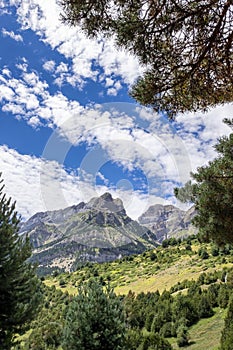 A mountain range framed with vegetation at the edges, on a summer day with a sky with cottony clouds, Pena Telera, Valle de Tena, photo