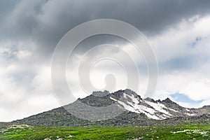 Mountain range with glaciers on slope under gloomy sky. Rainy gray clouds over snowy cliffs. Planning climb to top