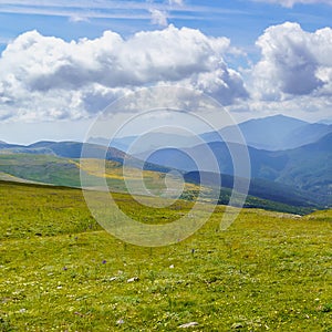 Mountain range with green meadows, flowers and blue sky with big white clouds. Relaxing and peaceful nature scene. Spanish