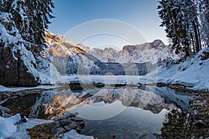 Mountain range Mangart reflecting in thawed part of lake Fusine