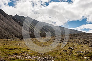Mountain range and mountainside with stones and green grass.