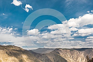 Mountain range under blue sky with cumulus clouds. Rocks and cliffs on horizon on sunny day