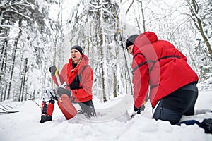 Mountain rescue service on operation outdoors in winter in forest, digging snow with shovels.