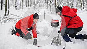 Mountain rescue service on operation outdoors in winter in forest, digging snow with shovels.