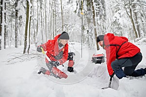 Mountain rescue service on operation outdoors in winter in forest, digging snow with shovels.