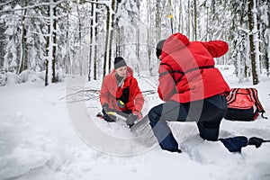 Mountain rescue service on operation outdoors in winter in forest, digging snow with shovels.