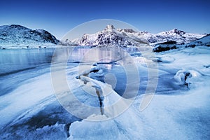 Mountain ridge and ice on the frozen lake surface. Natural landscape on the Lofoten islands, Norway.