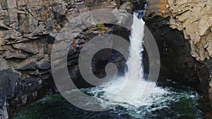 Mountain river falls in gorge. Waterfall flows down from cliff