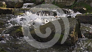 The mountain river flows among large stones covered with moss. Boiling water.