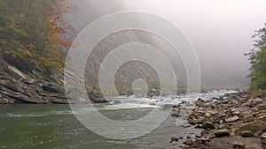 Mountain river in fog. Autumn landscape with rocky shore under cliff