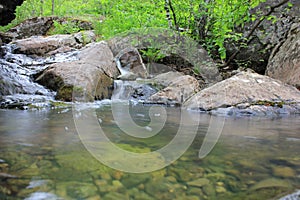 Mountain river - a small waterfall on a river with crystal clear water that flows among gray stones in a green forest on