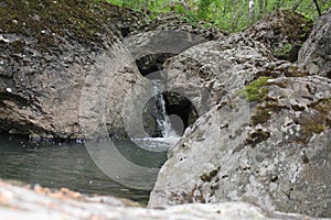 Mountain river - a small waterfall on a river with crystal clear water that flows among gray stones in a green forest on