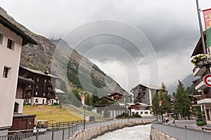 Mountain river in a village in Swiss Alps. Traditional wooden alpine houses. Sky before a thunderstorm.