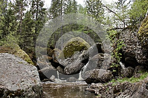 A mountain river waterfall flows through a river bed through huge boulders with moss