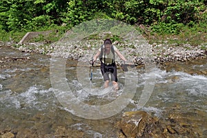 Mountain river. Young woman crossing the cold water