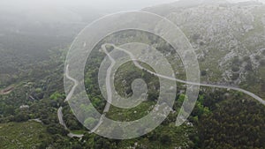 MOUNTAIN ROAD WITH DANGEROUS CURVES SURROUNDED BY FOREST FROM DRONE AERIAL VIEW