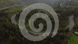 MOUNTAIN ROAD WITH DANGEROUS CURVES SURROUNDED BY FOREST FROM DRONE AERIAL VIEW