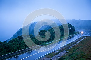 Mountain road in foggy dusk, motorcycle riding on asphalt road through the mountain top of Phnom Bokor Mountain in rainy day,