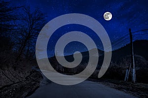 Mountain Road through the forest on a full moon night. Scenic night landscape of country road at night with large moon. Long