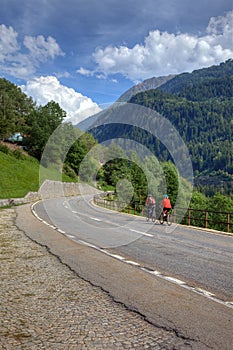 Mountain road landscape Swiss Alps mountains cyclists bicycle blue sky white clouds green forest trees summer travel highway rural