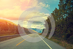 Mountain road at sunset with cloudy sky.