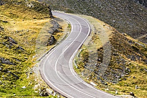 Mountain road winding through grass and scree hillside.