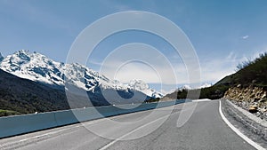 Mountain road winding through highland with trees and clouds in the sky