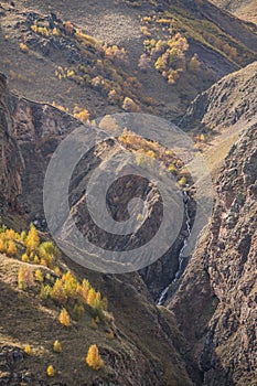 Mountain rocky slopes with a river and yellowed trees in autumn