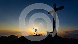 Mountain runner comes to the top where there is a cross at sunset