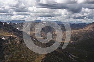 Mountain snow ranges and dramatic valley on the background of cloudy gloom dark sky