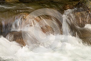 Mountain stream crashing over river rocks with white water and brown hue stones