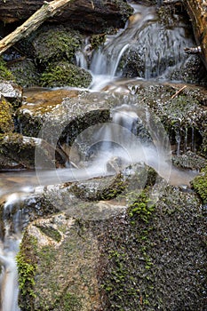 Mountain stream water flow with green moss on wet rocks. River cascade with huge stones.