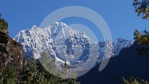 Mountain Thamserku in the Himalayas seen from Mount Everest Base Camp Trek near Manjo, Nepal framed by coniferous trees.