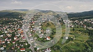 Mountain town on green grass hill aerial. Road with car at cottages. Nature landscape. Spring forest