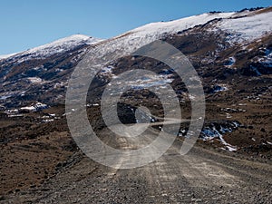 Mountain track off-road to a high-mountain village. Snow-covered narrow mountain road on the slope of snow mountains. Dangerous