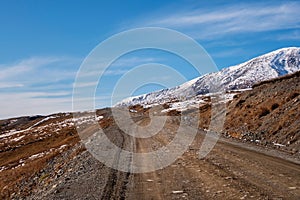 Mountain track off-road to a high-mountain village. Snow-covered narrow mountain road on the slope of snow mountains. Dangerous