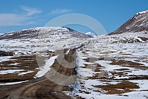 Mountain track off-road to a high-mountain village. Snow-covered narrow mountain road on the slope of snow mountains. Dangerous