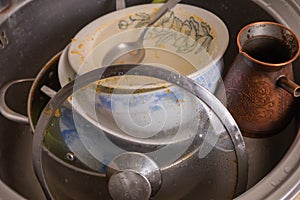 A mountain of unwashed utensils in a kitchen sink. Desolation and mess