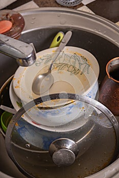 A mountain of unwashed utensils in a kitchen sink. Desolation and mess