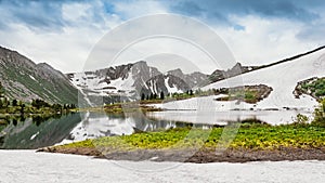 Mountain valley with snow forest and lake at foot. Rocks are reflected in river. Melting glacier on slopes of ridge