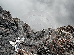 Mountain view from cliff at high altitude. Mystical landscape with beautiful sharp rocks near precipice and couloirs in low clouds