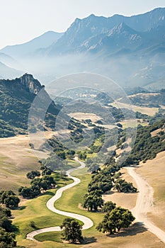 Mountain view landscape with winding pathway crossing the dry valley and passing under shaded trees on a bright sunny day with