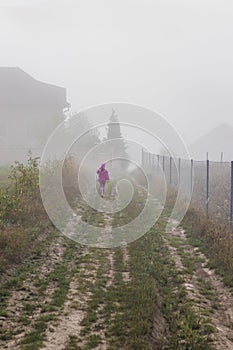 Mountain from view with small village and flow fog. Little girl in red and foggy summer morning in the mountains and a small