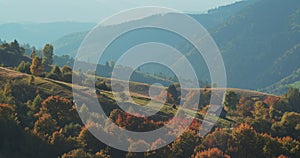 Mountain village with small houses surrounded by hills and mountains. Green mountain hills with yellow and red tree forest in fall