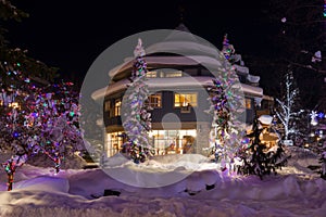 Mountain village after snowfall in night. Christmas illumination - trees, garlands and night lights, snow-covered houses, pine tre