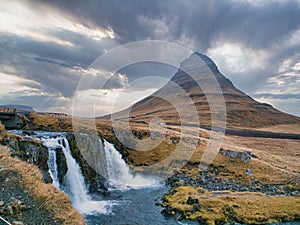 a mountain with waterfall and bridge going over it to a valley