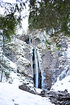 Mountain waterfall with rocks and cliffs covered with snow