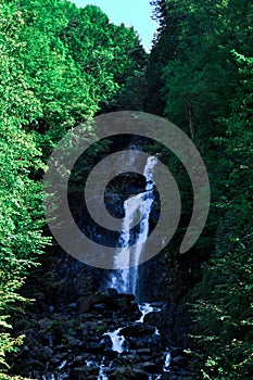 Mountain waterfall between stone rocks and green trees