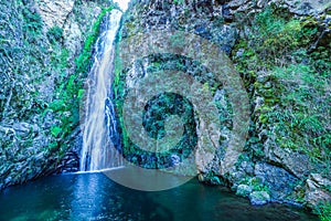 Mountain waterfall with white water in tropical forest among bare rocks