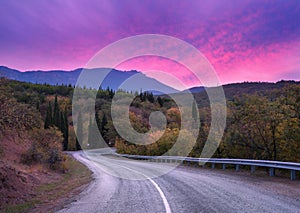 Mountain winding road passing through the forest with dramatic colorful sky and red clouds at dusk in summer